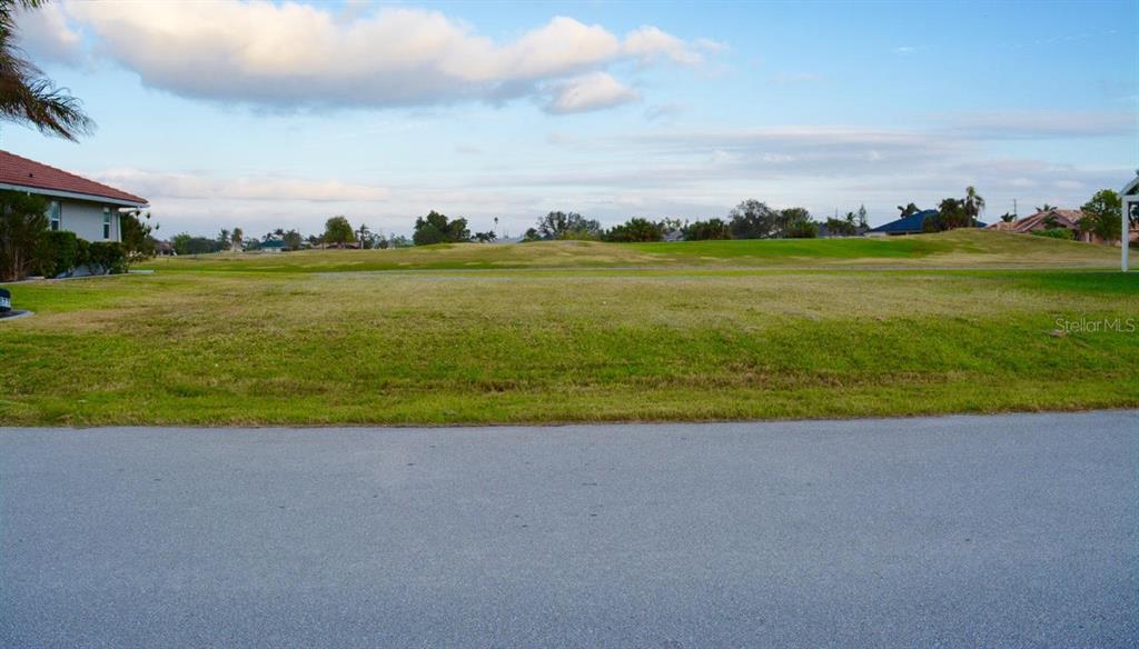 A vacant grassy lot sits adjacent to a residential street with houses in the background — 3880 BORDEAUX DRIVE, PUNTA GORDA, FL