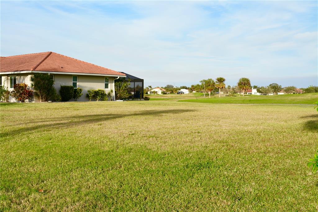 A grassy yard extends toward a house with a red tile roof and screened enclosure — 3880 BORDEAUX DRIVE, PUNTA GORDA, FL