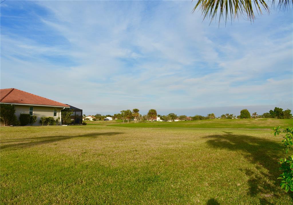 A grassy backyard overlooks a golf course next to a house with a tiled roof — 3880 BORDEAUX DRIVE, PUNTA GORDA, FL