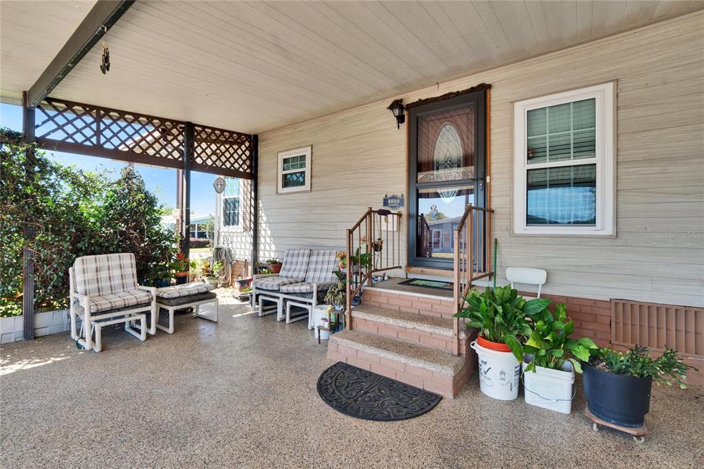 A covered porch features a brick-stepped entrance, outdoor furniture, and potted plants — 4910 LOCH NESS DRIVE, LAKELAND, FL