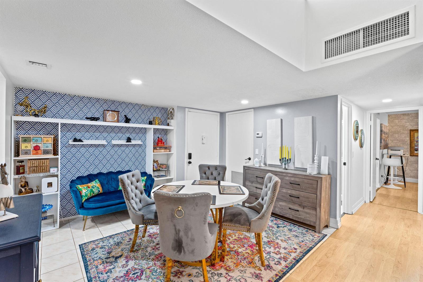 A dining area features a round table, grey tufted chairs, a blue sofa, and patterned wallpaper — 2540 Boundbrook Boulevard # 209, Palm Springs FL 33406, PALM SPRINGS, FL