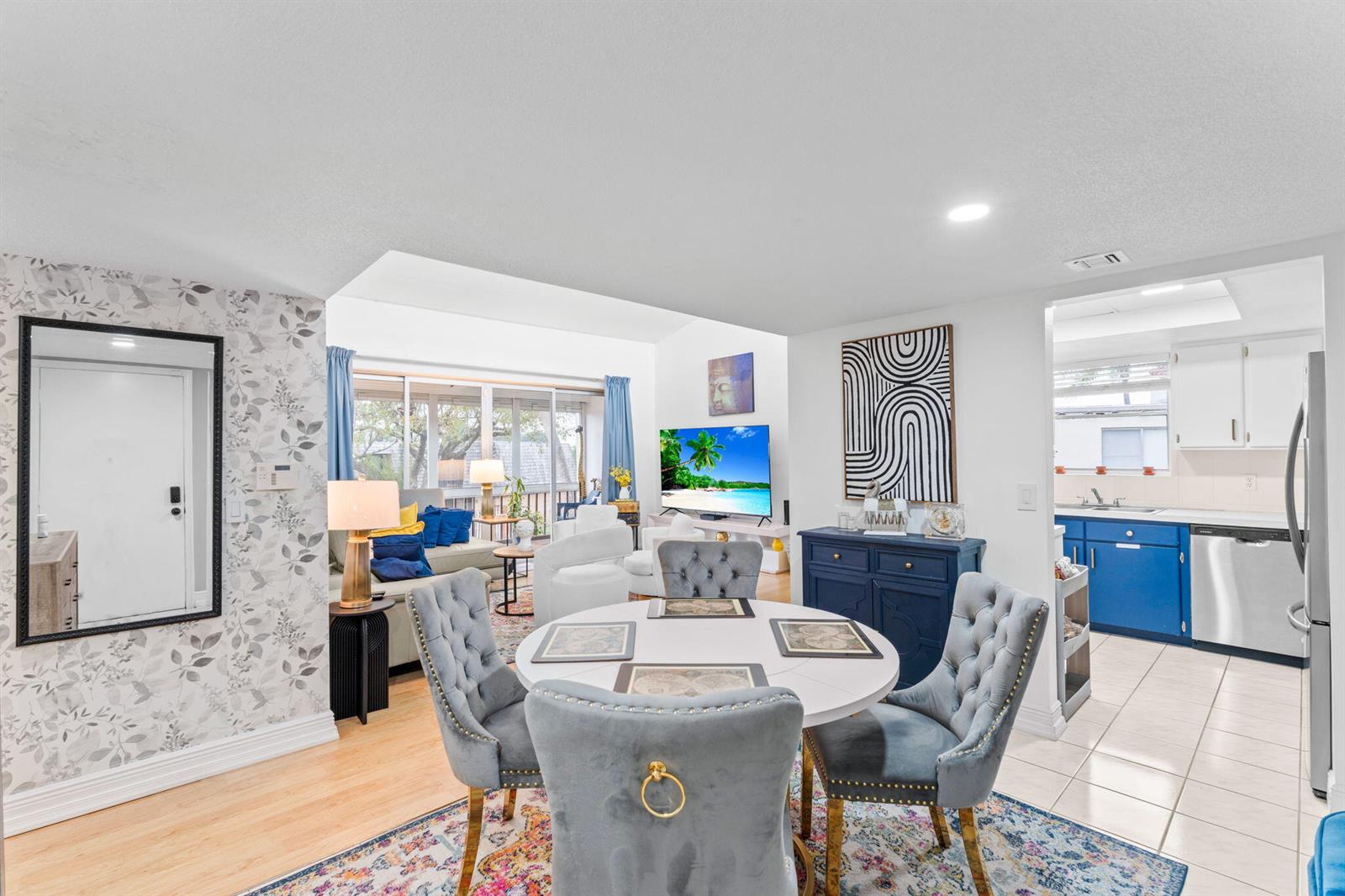 A dining area with tufted chairs sits before a living room and a blue-cabinet kitchen — 2540 Boundbrook Boulevard # 209, Palm Springs FL 33406, PALM SPRINGS, FL
