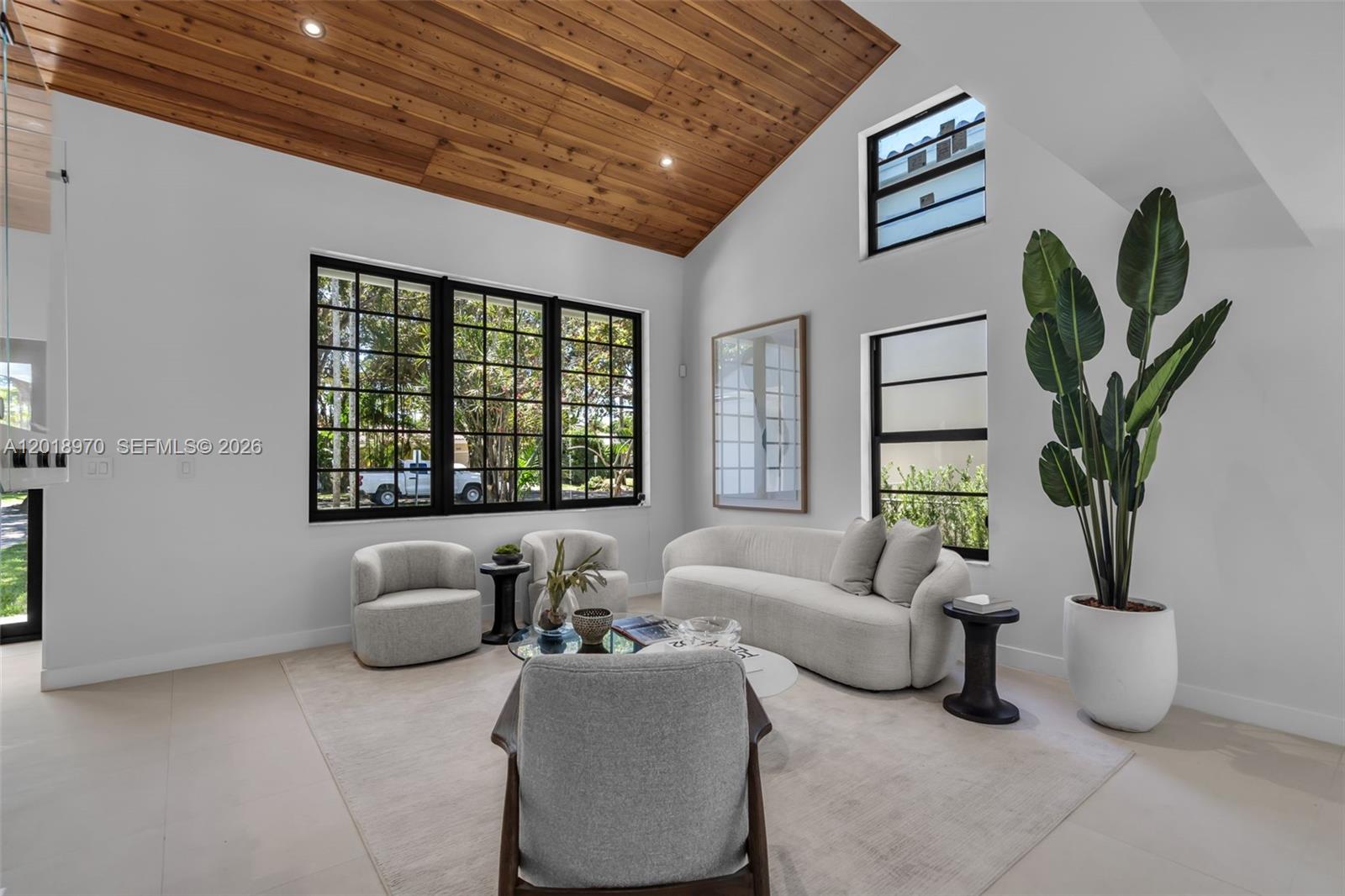 A living room features a vaulted wood-paneled ceiling, white walls, and large black-framed windows — 1415 Trillo Ave, Coral Gables FL 33146, CORAL GABLES, FL