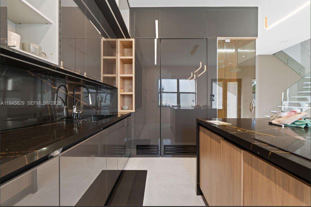 A modern kitchen features dark glossy cabinetry, black stone countertops with gold veining, and wood accents — 4499 SW 173rd Ave, Miramar FL 33029, MIRAMAR, FL