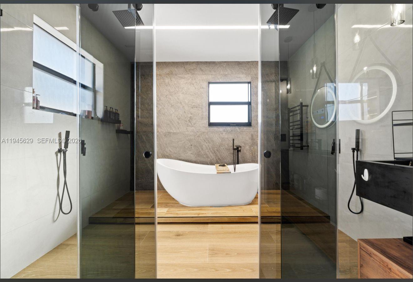 A modern bathroom features a freestanding white tub on a wooden platform behind glass doors — 4499 SW 173rd Ave, Miramar FL 33029, MIRAMAR, FL