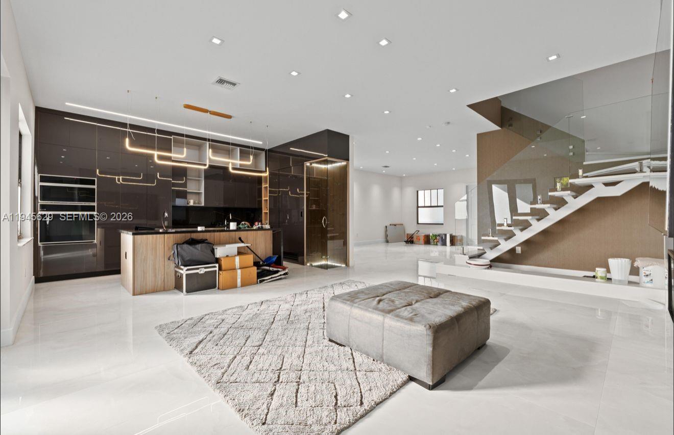 A modern open-concept kitchen and living area with glossy cabinets, a staircase, and tile flooring — 4499 SW 173rd Ave, Miramar FL 33029, MIRAMAR, FL