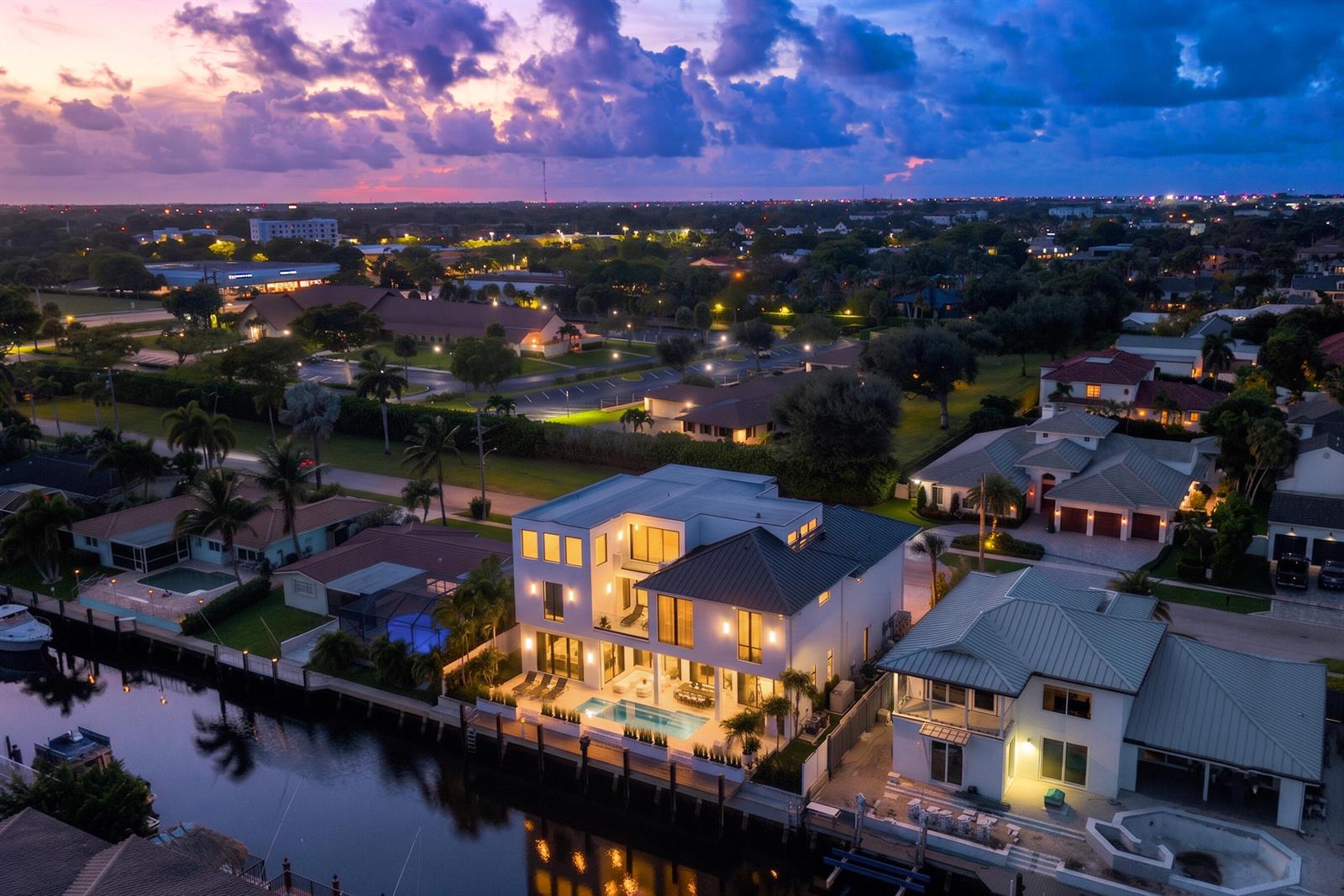 An aerial view of a modern three-story waterfront home with a pool at dusk — 748 NE 72nd Street, Boca Raton FL 33487, BOCA RATON, FL