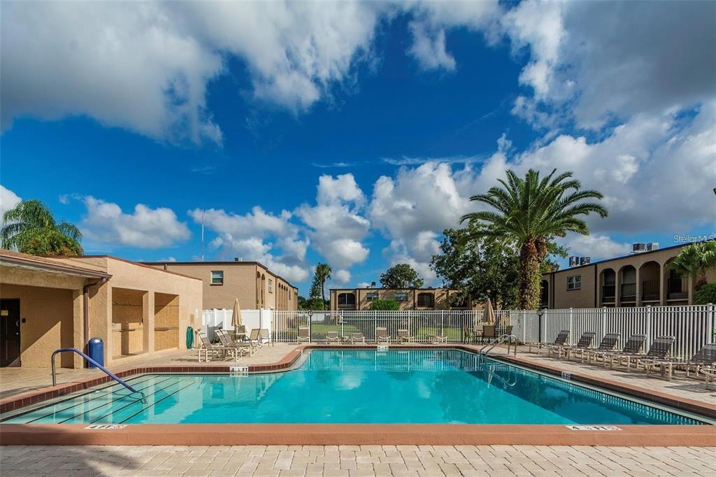 An outdoor swimming pool surrounded by lounge chairs, a white fence, and apartment buildings — 7701 STARKEY ROAD UNIT 521, SEMINOLE, FL