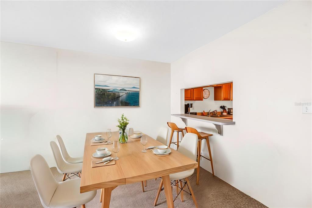 A dining room with a wooden table, white chairs, and a pass-through window to the kitchen — 7701 STARKEY ROAD UNIT 521, SEMINOLE, FL