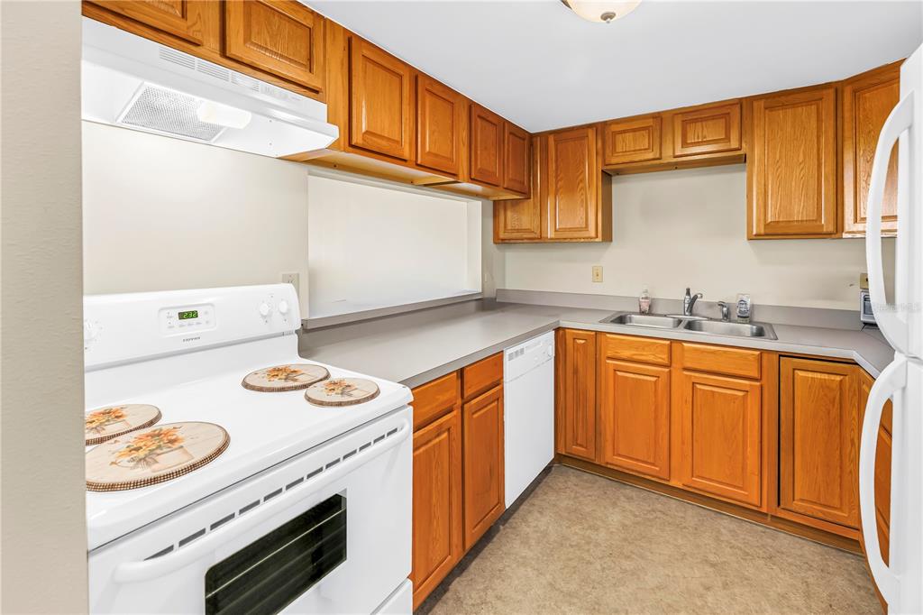 A kitchen with wood cabinets, white appliances, and a double sink under a pass-through window — 7701 STARKEY ROAD UNIT 521, SEMINOLE, FL