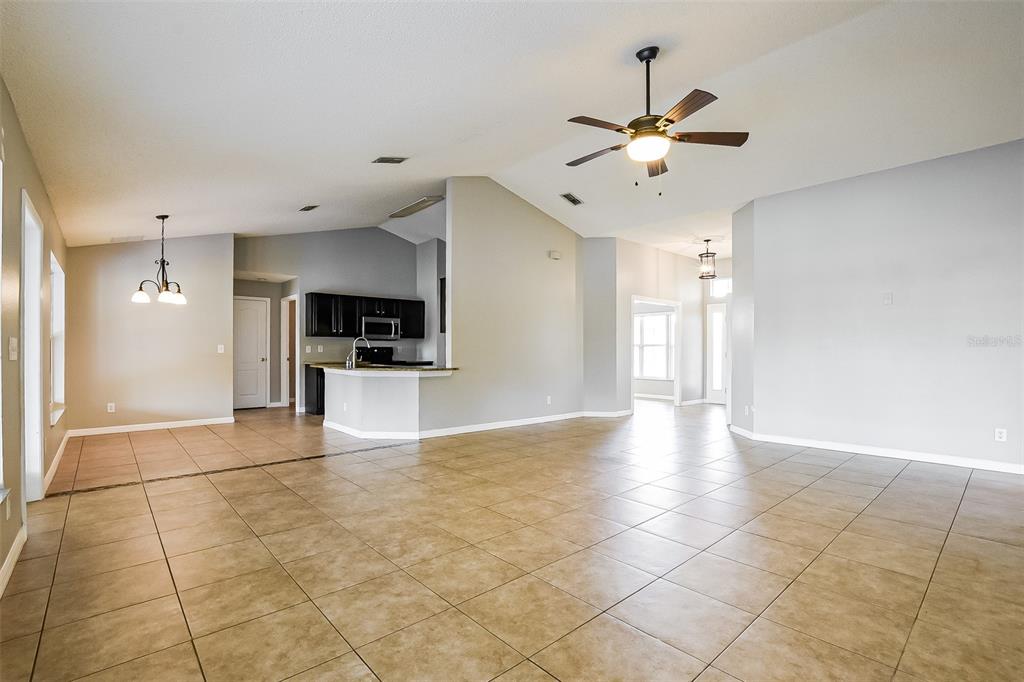 An open-concept living area features tan tile flooring, a ceiling fan, and a kitchen peninsula — 2091 FAWN MEADOW CIRCLE, ST CLOUD, FL