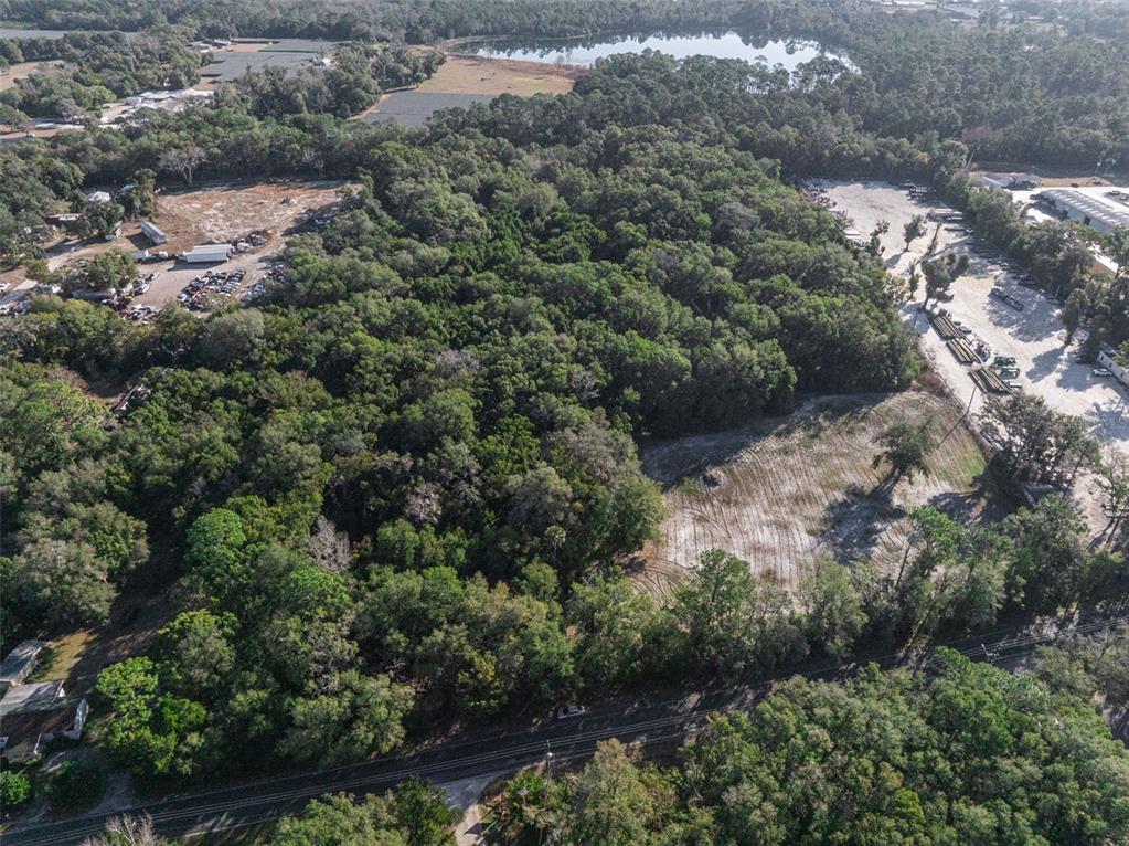 An aerial view shows a wooded lot bordered by a road, industrial areas, and water — 589 S VOLUSIA AVENUE, PIERSON, FL