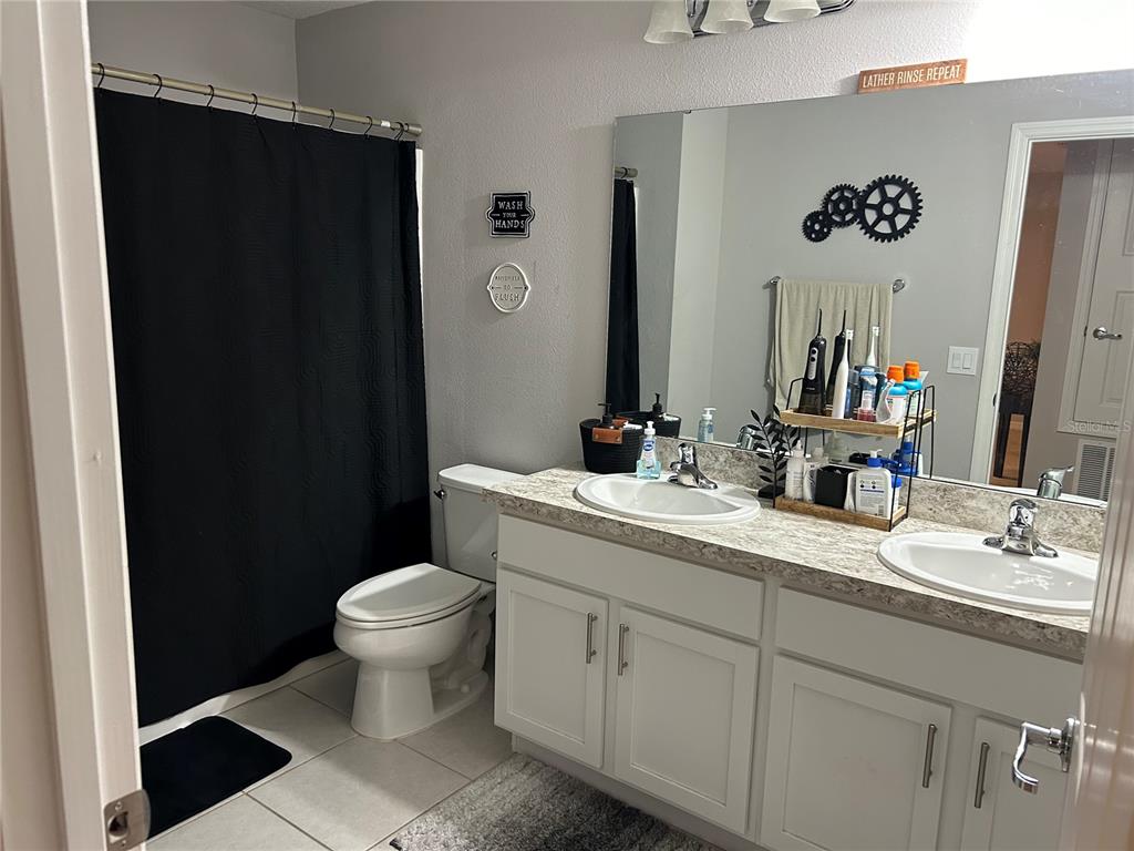 A bathroom features a double vanity with white cabinets, a toilet, and a shower curtain — 3363 BELLEZZA COURT, KISSIMMEE, FL