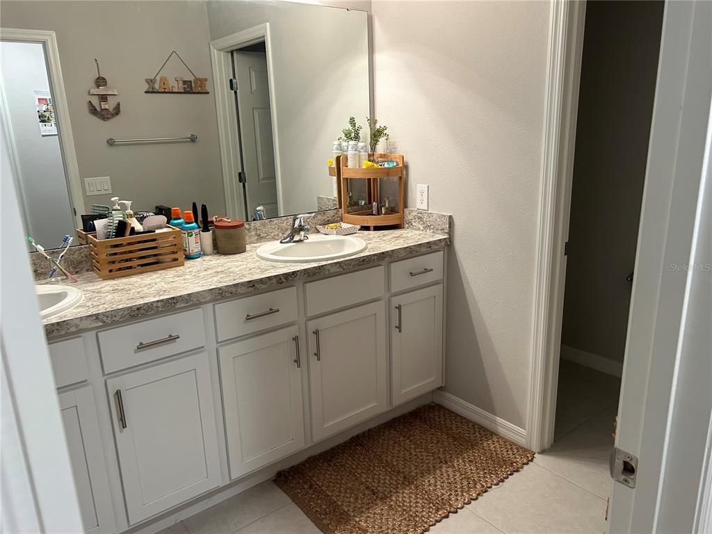 A bathroom features a white vanity with a stone countertop, a mirror, and tiled flooring — 3363 BELLEZZA COURT, KISSIMMEE, FL