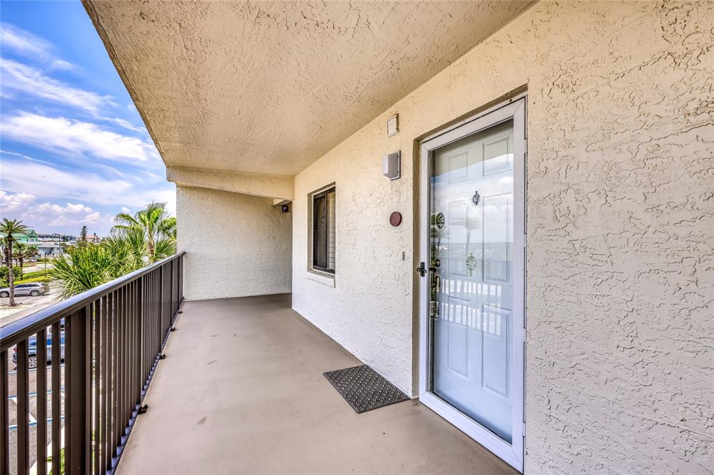 An outdoor balcony features a white door, a black metal railing, and a textured wall — 6727 TURTLEMOUND ROAD UNIT 318, NEW SMYRNA BEACH, FL