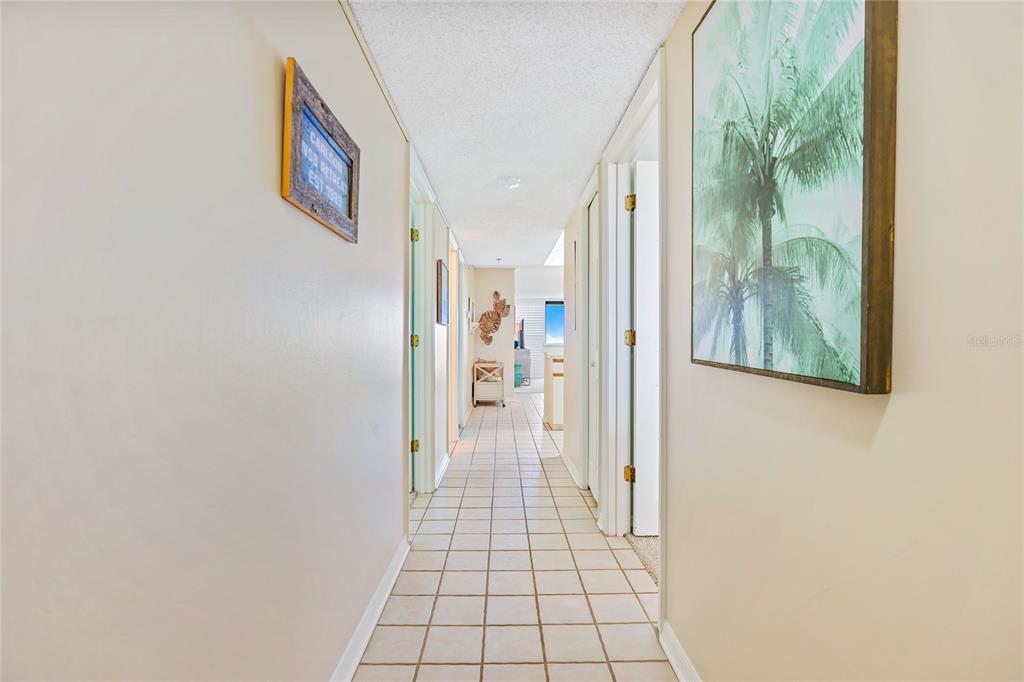 A tiled hallway leads toward a bright living area with a palm tree wall art piece — 6727 TURTLEMOUND ROAD UNIT 318, NEW SMYRNA BEACH, FL
