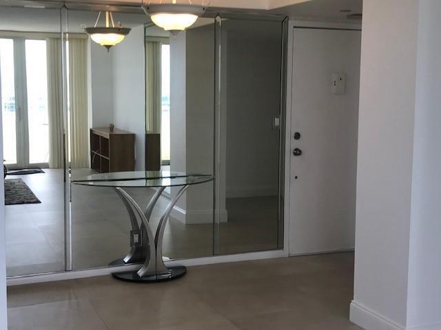 A modern entryway features a glass console table against a mirrored wall and white door — 111 Briny Avenue # 14, Pompano Beach FL 33062, POMPANO BEACH, FL