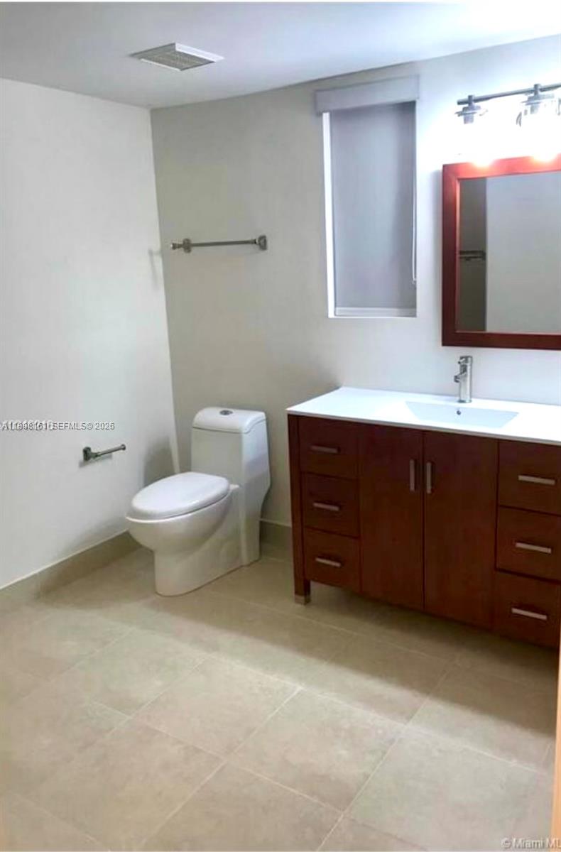 A bathroom features a white toilet, a wooden vanity with a white countertop, and a mirror — 55 E 4th St # 102, Hialeah FL 33010, HIALEAH, FL