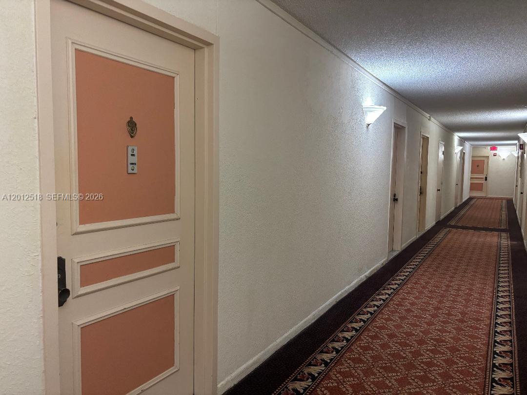 A long hotel hallway features a patterned carpet, white walls, and several closed doors — 600 Three Islands Blvd # 1003, Hallandale Beach FL 33009, HALLANDALE BEACH, FL