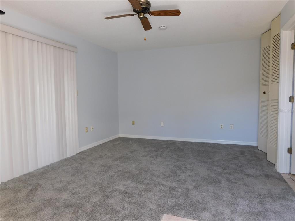 An empty bedroom features light blue walls, gray carpeting, a ceiling fan, and closet doors — 1118 SPRING MEADOW DRIVE, KISSIMMEE, FL