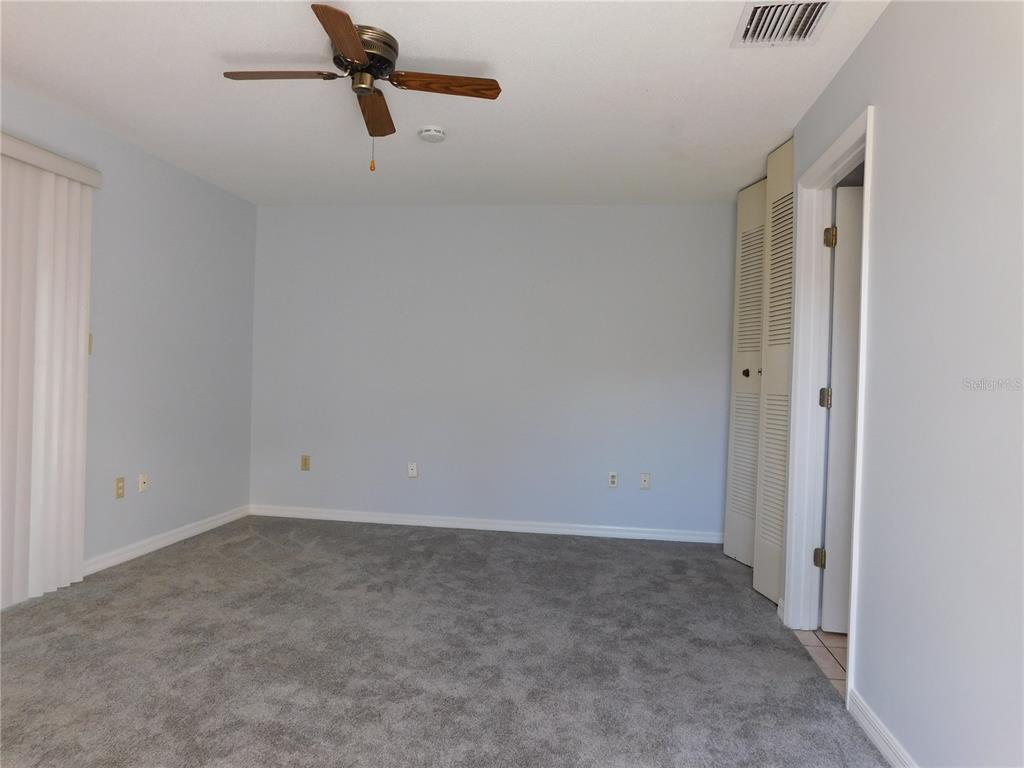 A bedroom with light blue walls, gray carpeting, a ceiling fan, and louvered closet doors — 1118 SPRING MEADOW DRIVE, KISSIMMEE, FL
