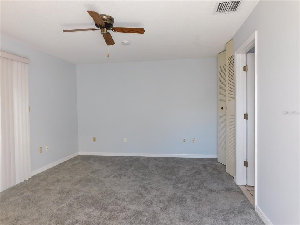 An empty bedroom features light blue walls, gray carpeting, a ceiling fan, and louvered closet doors — 1118 SPRING MEADOW DRIVE, KISSIMMEE, FL