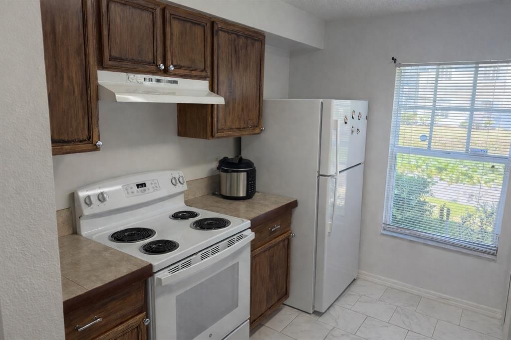 A kitchen features wood cabinets, white appliances, tiled countertops, and a window with blinds — 7135 WATERSIDE DRIVE, TAMPA, FL
