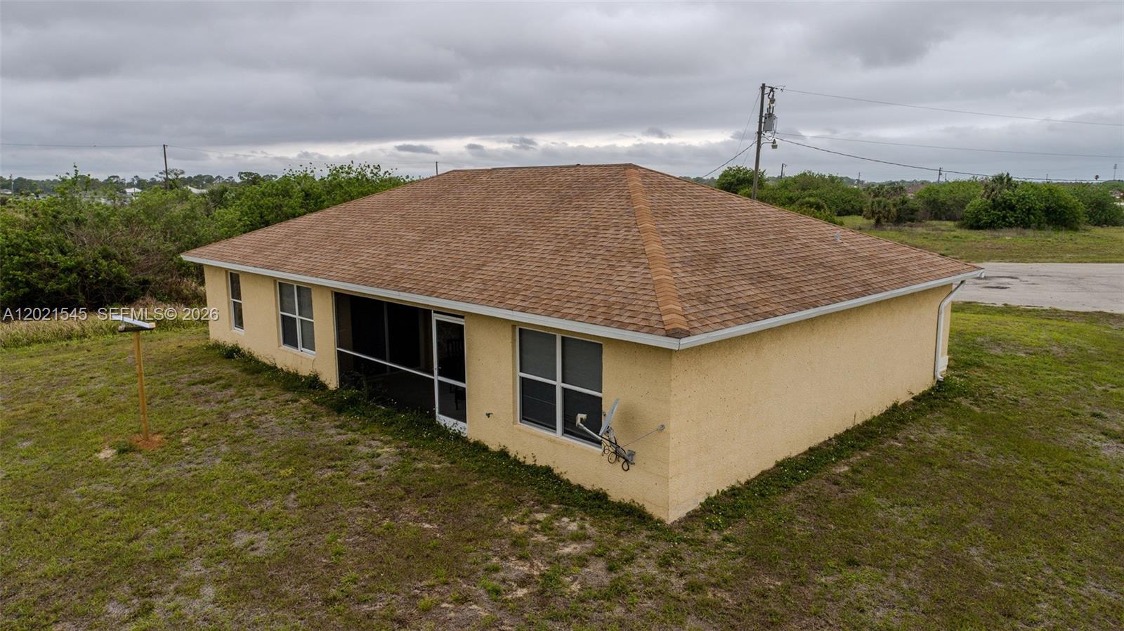 An aerial view of the rear exterior of a yellow house with a screened porch — 7018 PILGRIM CT, La Belle FL 33935, LA BELLE, FL