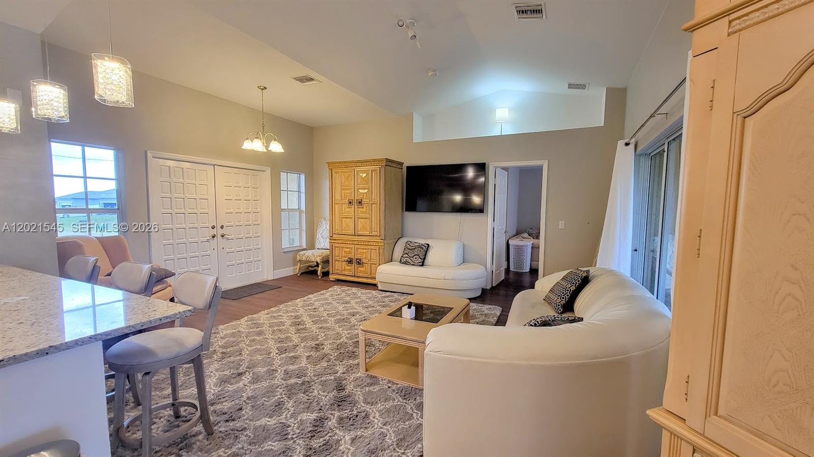 A living room features a white sofa, a large area rug, and a wall-mounted television — 7018 PILGRIM CT, La Belle FL 33935, LA BELLE, FL