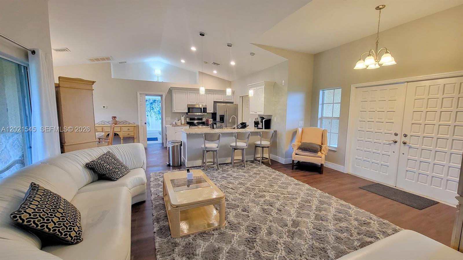 This open-concept living room features a white kitchen, a gray area rug, and vaulted ceilings — 7018 PILGRIM CT, La Belle FL 33935, LA BELLE, FL