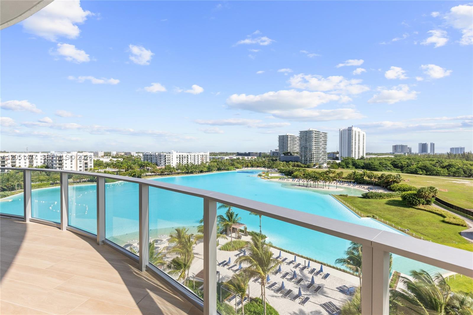 A balcony with a glass railing overlooks a large turquoise lagoon and surrounding landscape — 2411 Laguna Cr # 611, Miami FL 33181, MIAMI, FL
