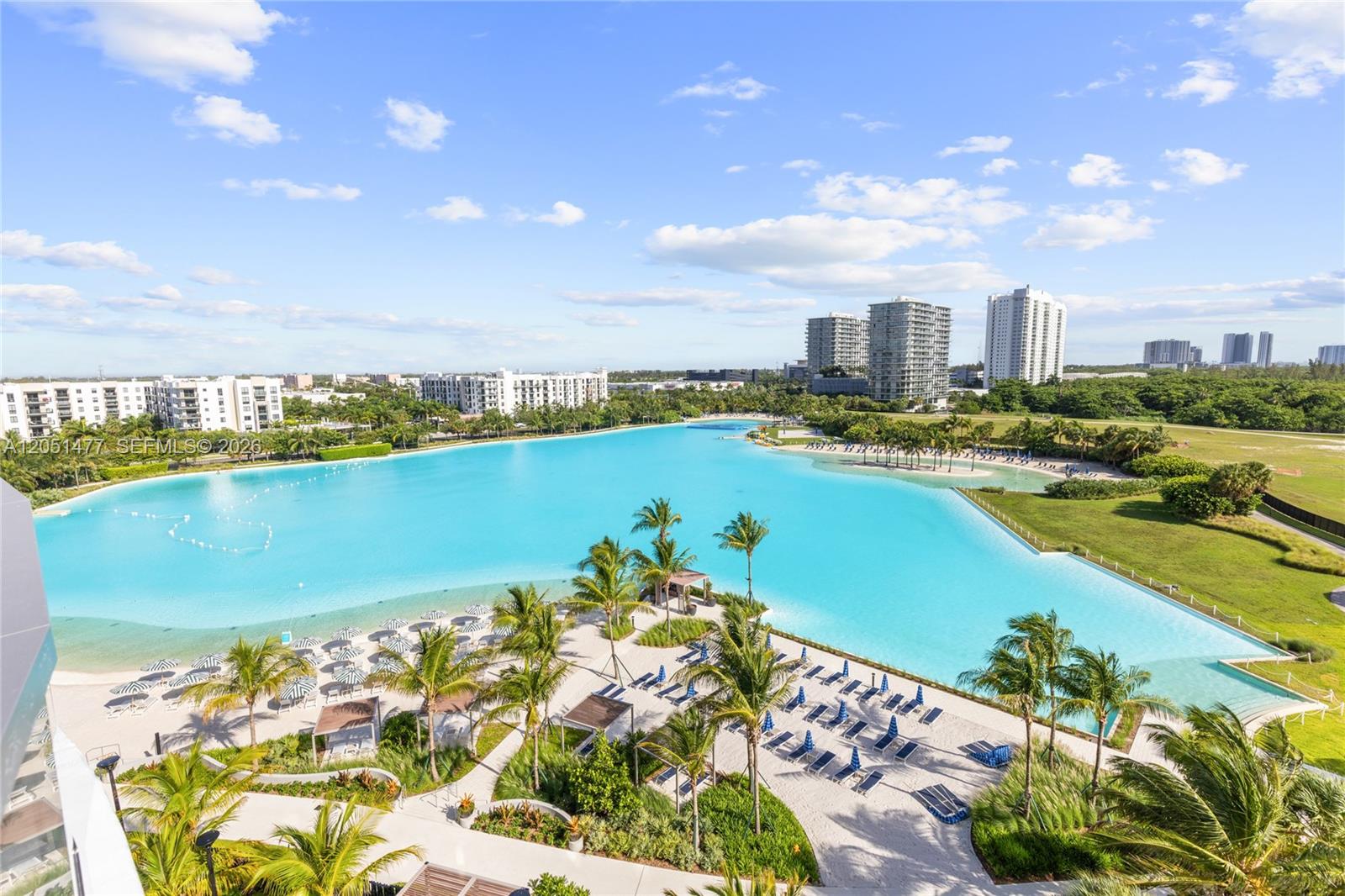 An aerial view shows a large turquoise lagoon surrounded by palm trees, lounge chairs, and buildings — 2411 Laguna Cr # 611, Miami FL 33181, MIAMI, FL