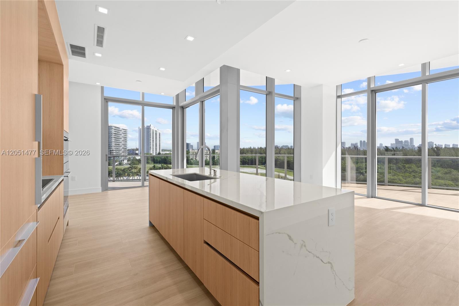 A modern kitchen features light wood cabinetry, a marble-topped island, and floor-to-ceiling windows — 2411 Laguna Cr # 611, Miami FL 33181, MIAMI, FL