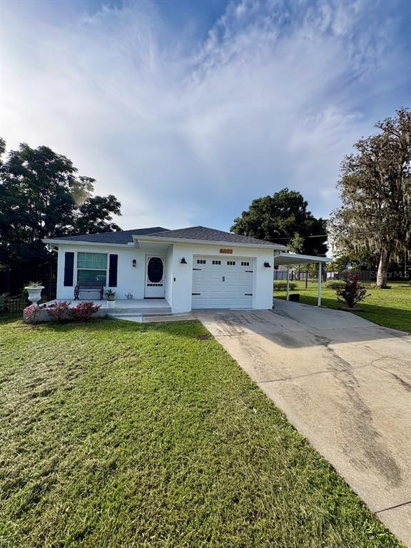 A white single-story house with a garage and a concrete driveway under a blue sky — 6022 POLK AVENUE NW, LAKELAND, FL