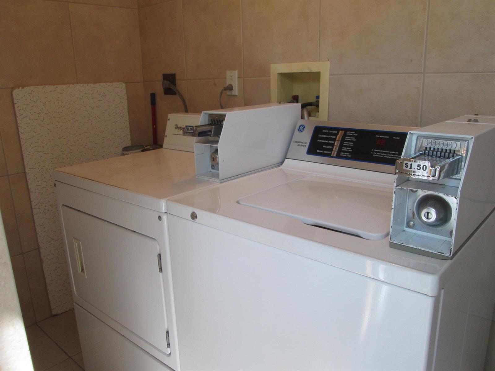 A laundry room features a white coin-operated washing machine and dryer against tiled walls — 405 N Cypress Drive # 8, Jupiter FL 33469, JUPITER, FL