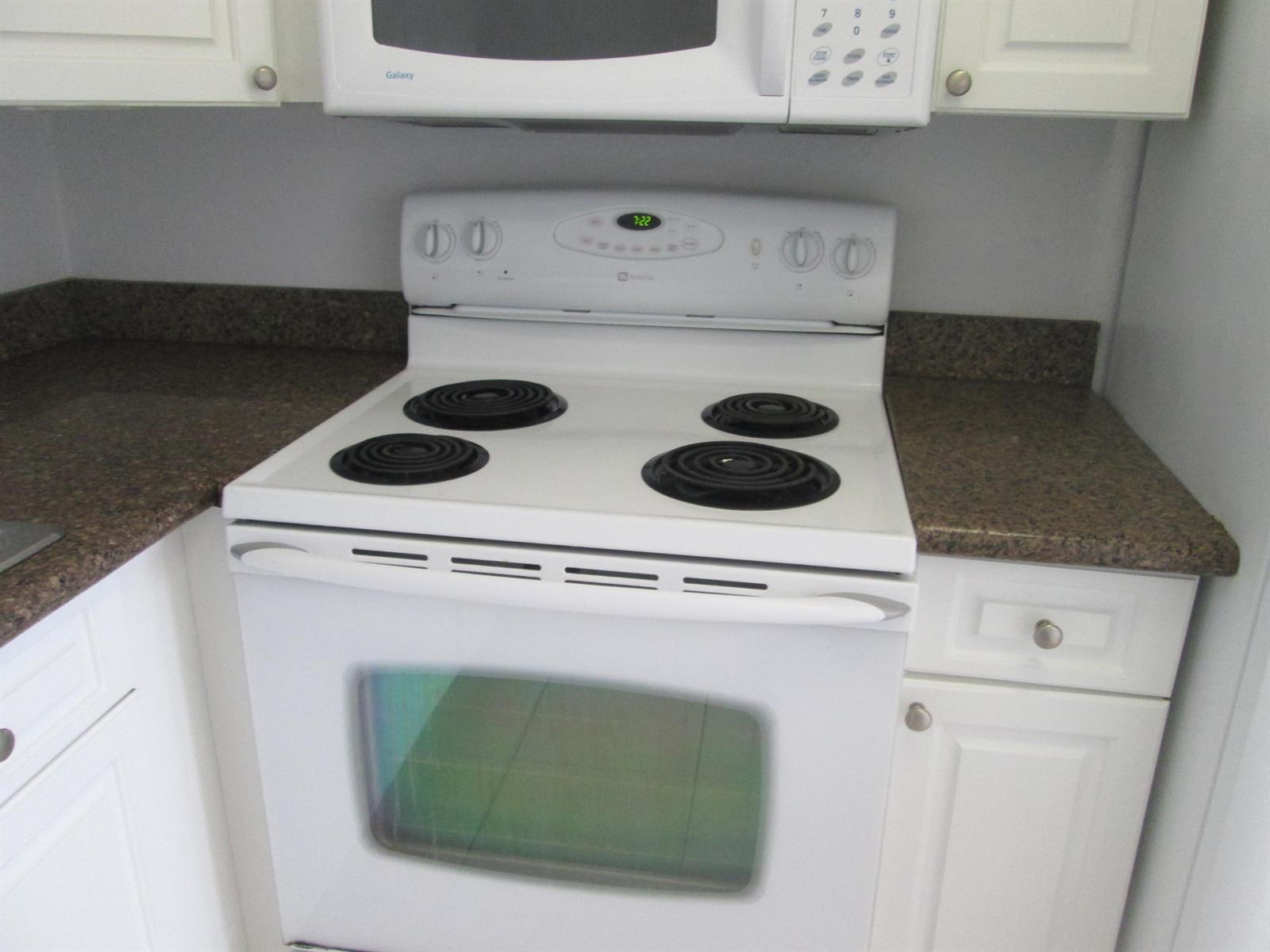 A white electric range sits between white cabinets and brown speckled countertops in a kitchen — 405 N Cypress Drive # 8, Jupiter FL 33469, JUPITER, FL