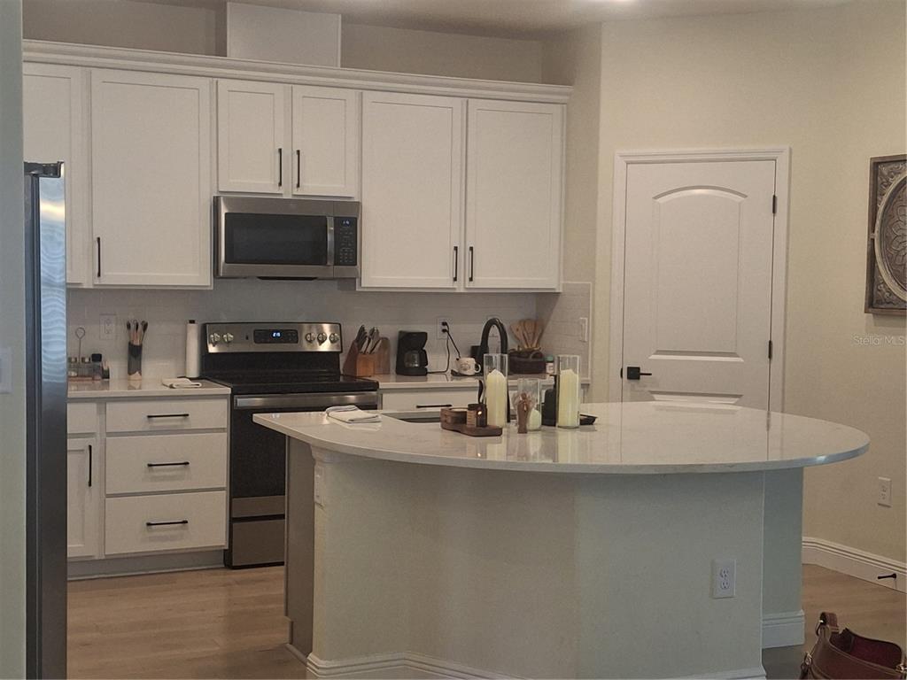 A kitchen features white cabinets, stainless steel appliances, and a large curved quartz island — 12618 VANDER WAY, NEW PORT RICHEY, FL