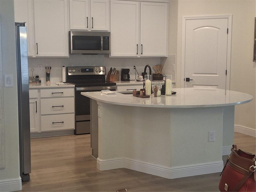 A kitchen features white cabinets, stainless steel appliances, and a curved quartz-topped island — 12618 VANDER WAY, NEW PORT RICHEY, FL