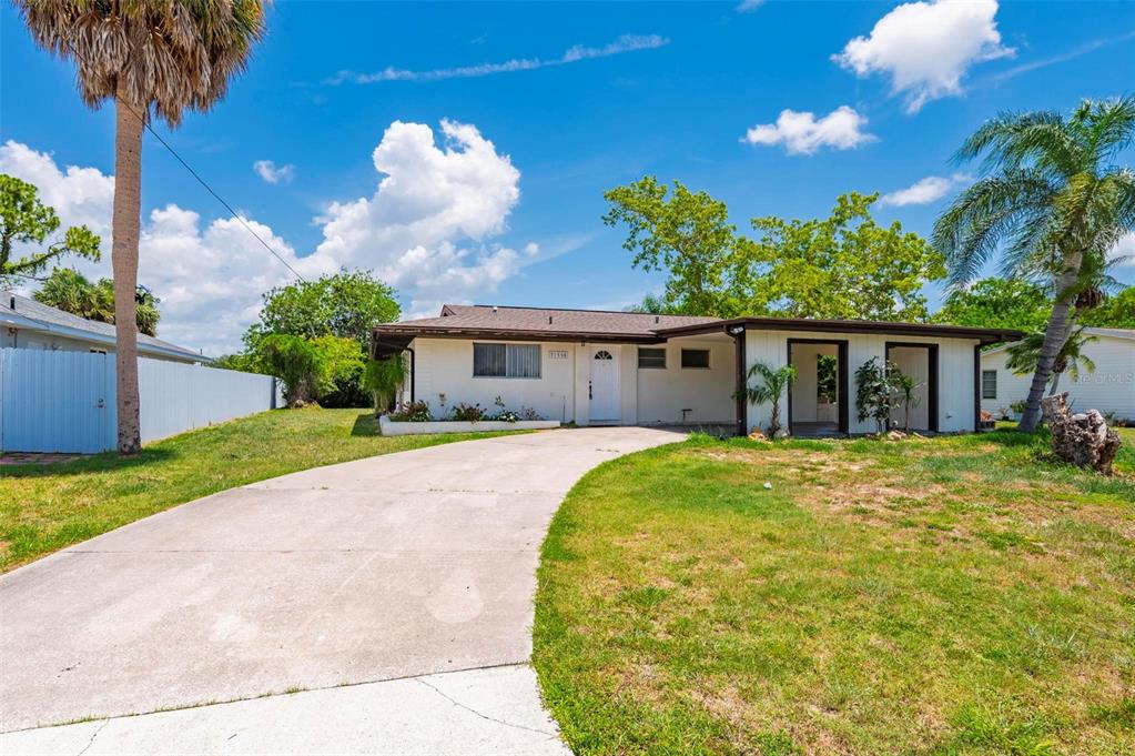 A single-story house with a concrete driveway, white exterior, and a palm tree in front — 21358 BURKHART DRIVE, PORT CHARLOTTE, FL