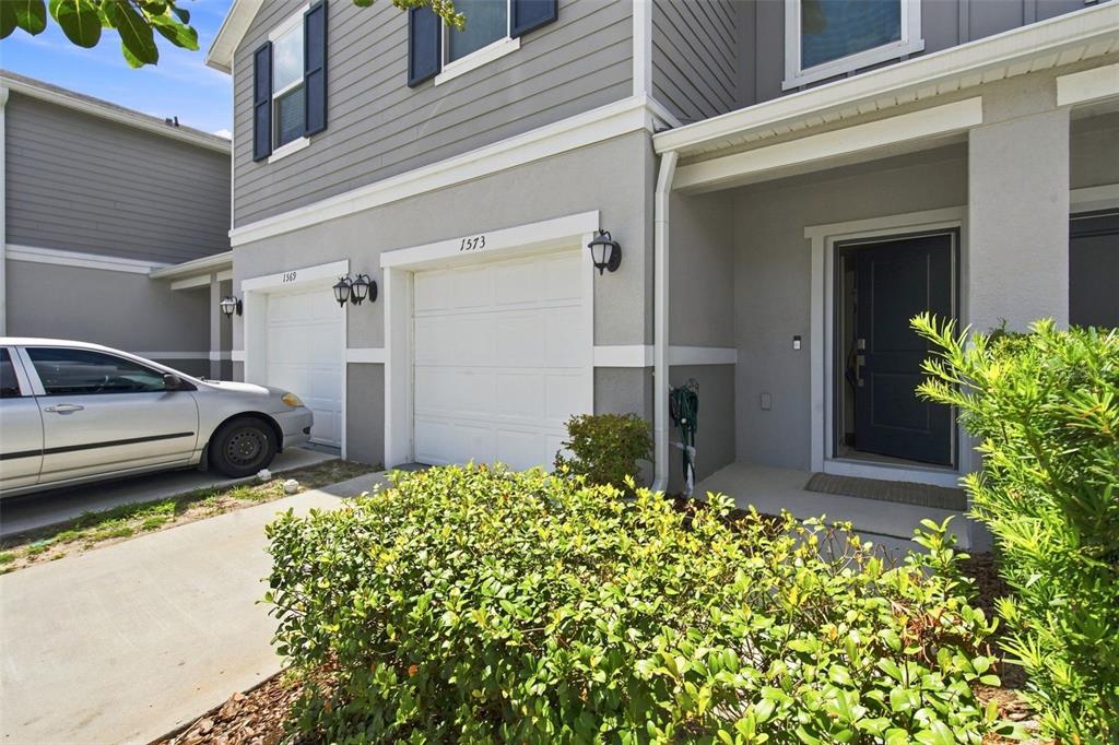 A two-story townhouse exterior features a white garage door, a dark front door, and landscaping — 1573 MIRABELLA CIRCLE, DAVENPORT, FL