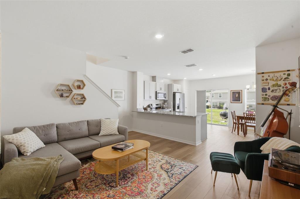 An open-concept living room and kitchen featuring a grey sectional, wood floors, and dining area — 1573 MIRABELLA CIRCLE, DAVENPORT, FL