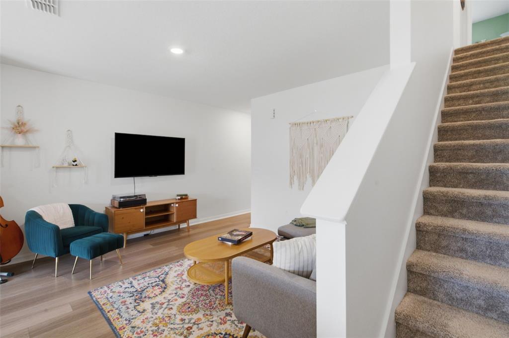 A living room features a mounted television, a teal armchair, a coffee table, and stairs — 1573 MIRABELLA CIRCLE, DAVENPORT, FL