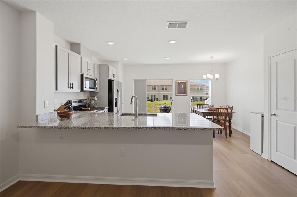 A kitchen with granite countertops and white cabinets overlooks a dining area and backyard — 1573 MIRABELLA CIRCLE, DAVENPORT, FL