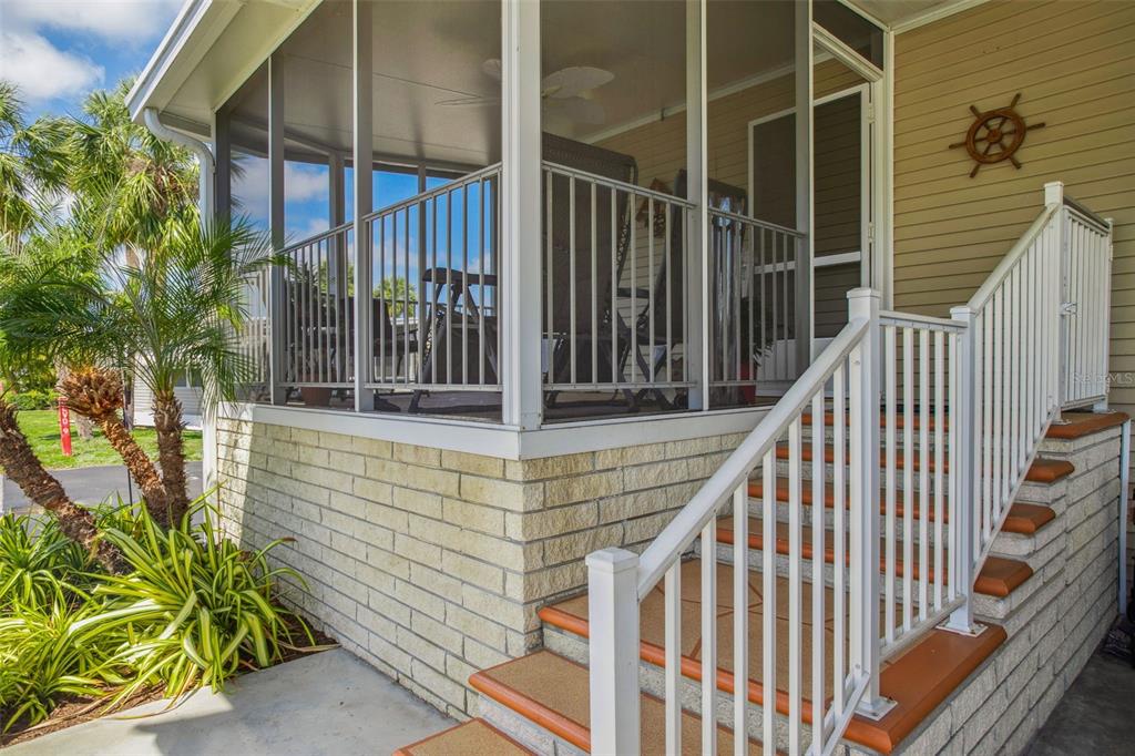 A screened-in porch with white railings sits above brick steps leading to a house entrance — 4851 W GANDY BOULEVARD UNIT B09L23, TAMPA, FL
