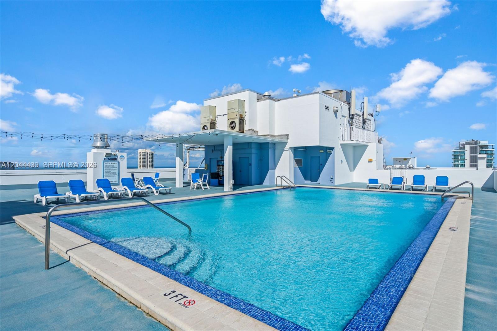 A rooftop swimming pool with blue lounge chairs and a white building structure — 401 69th St # 1012, Miami Beach FL 33141, MIAMI BEACH, FL