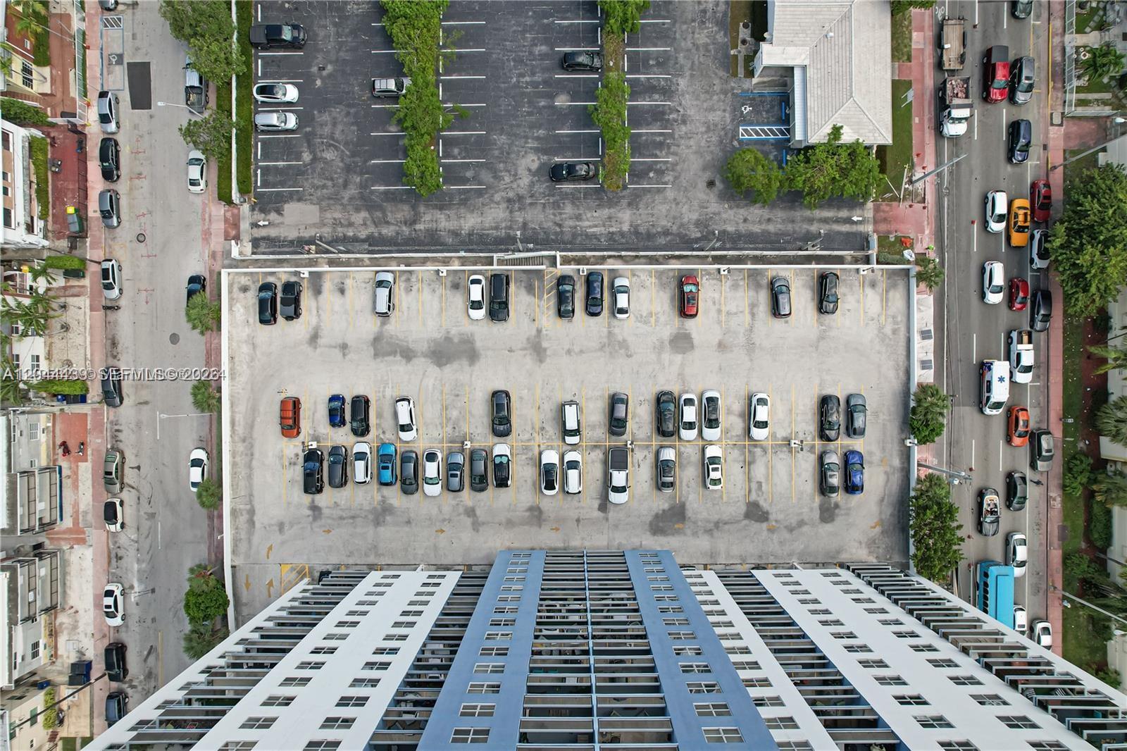 An aerial view shows a high-rise building with an adjacent parking lot and street traffic — 401 69th St # 1012, Miami Beach FL 33141, MIAMI BEACH, FL