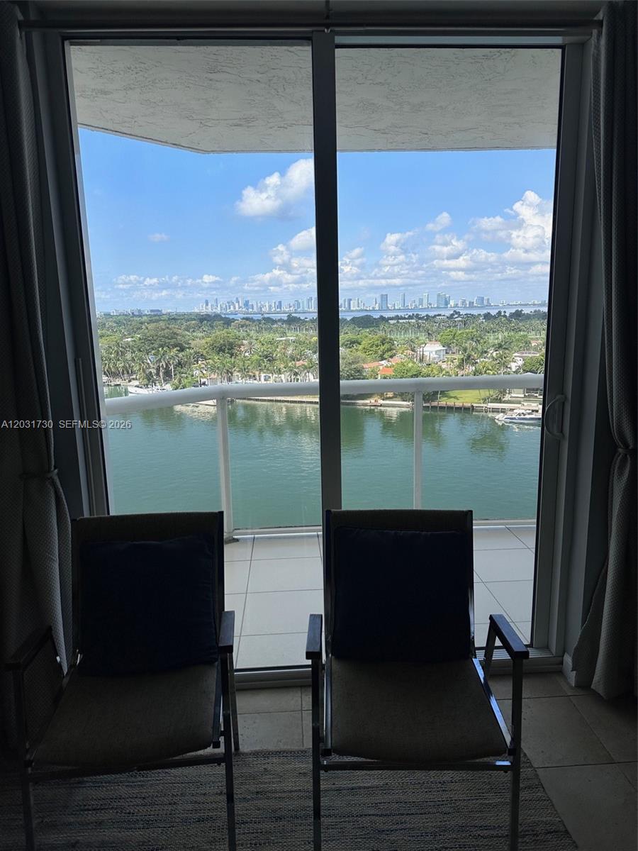 Two chairs face a balcony overlooking a waterway and a distant city skyline — 5880 W Collins Ave # 1203, Miami Beach FL 33140, MIAMI BEACH, FL