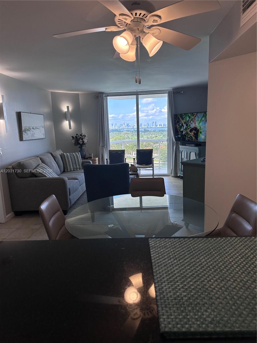 A dining area with a glass table overlooks a living room and a balcony view — 5880 W Collins Ave # 1203, Miami Beach FL 33140, MIAMI BEACH, FL