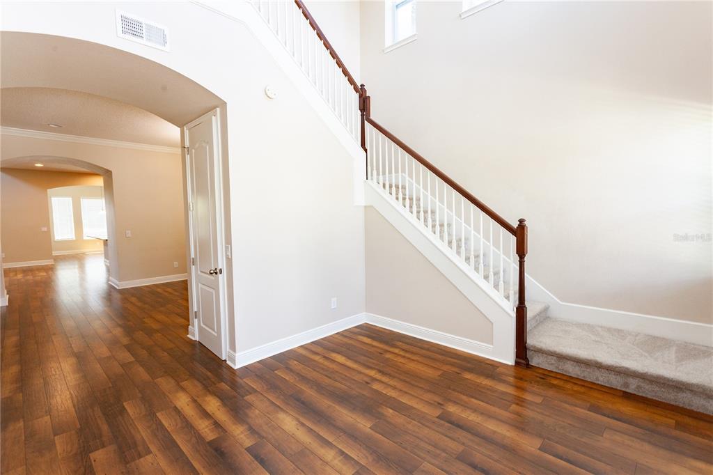 An interior view shows a foyer with wood flooring, a carpeted staircase, and an arched entryway — 8202 BELLOW STREET, ORLANDO, FL