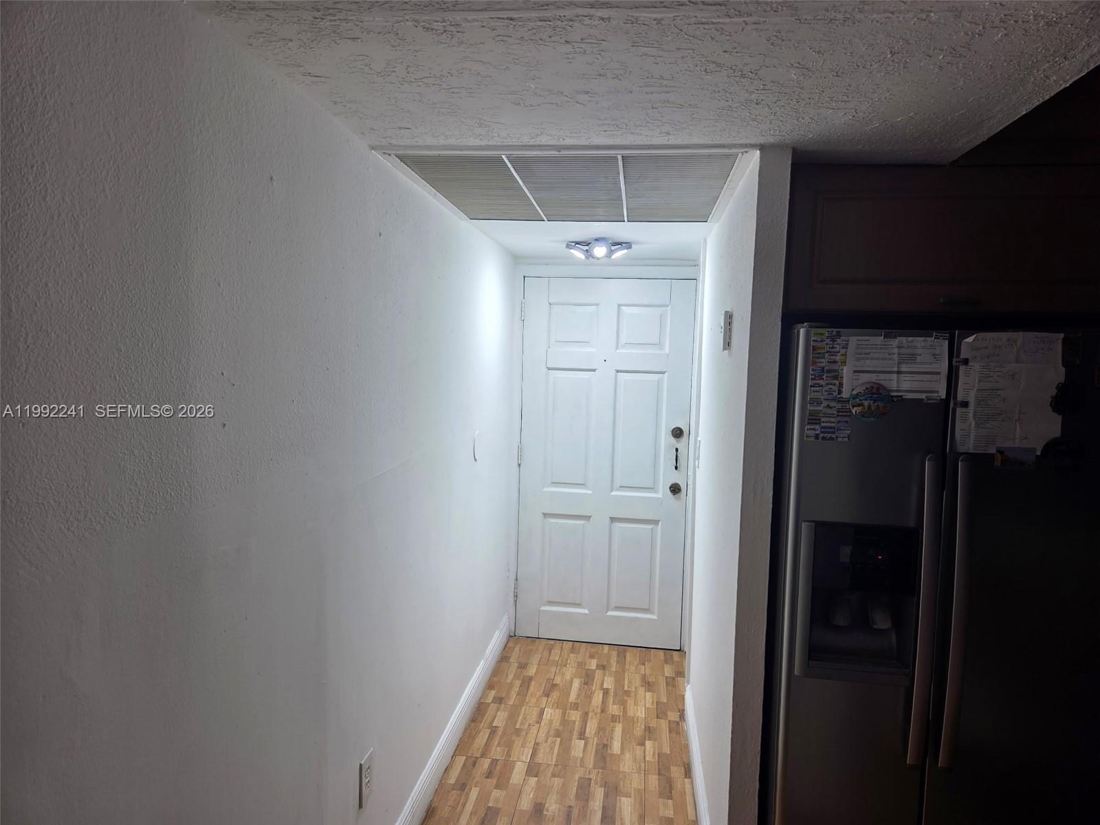 A white door sits at the end of a narrow hallway with wood-look flooring — 6580 W Flagler St # 101, Miami FL 33144, MIAMI, FL